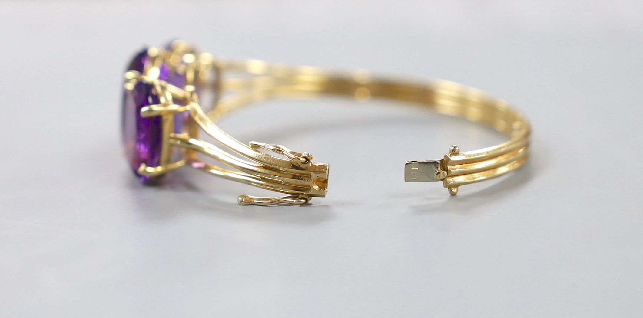 A modern 14k and three stone oval cut amethyst set hinged bangle, interior diameter 54mm, gross weight 24.8 grams.